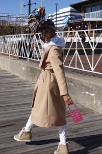 a woman in a tan coat walking on a boardwalk