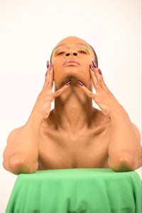 a woman with green paint on her face is laying on top of a green table