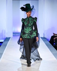 a woman wearing a green and black outfit on the runway